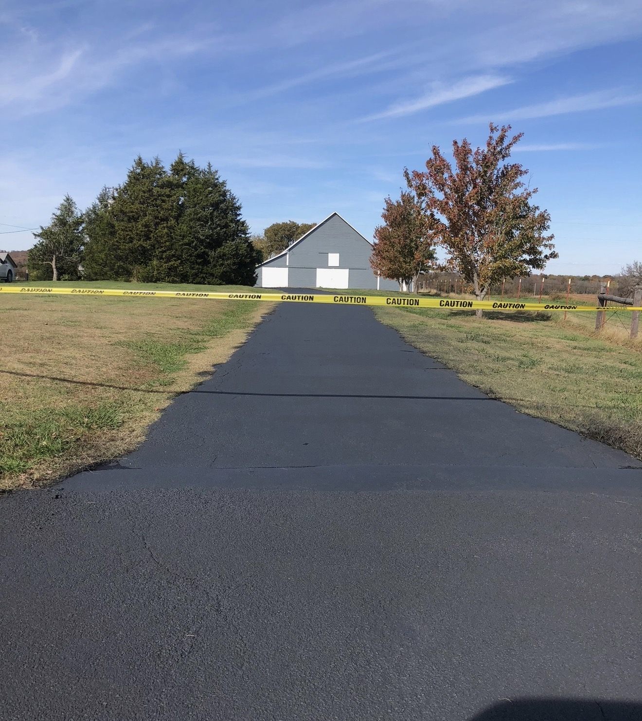 Newly sealed asphalt driveway taped off and curing in front of a residential garage